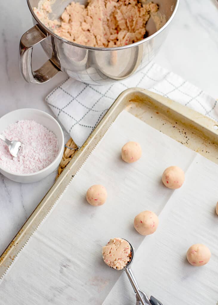 cookie scoop with dough on it sitting on a parchment lined baking sheet with snowball cookie dough