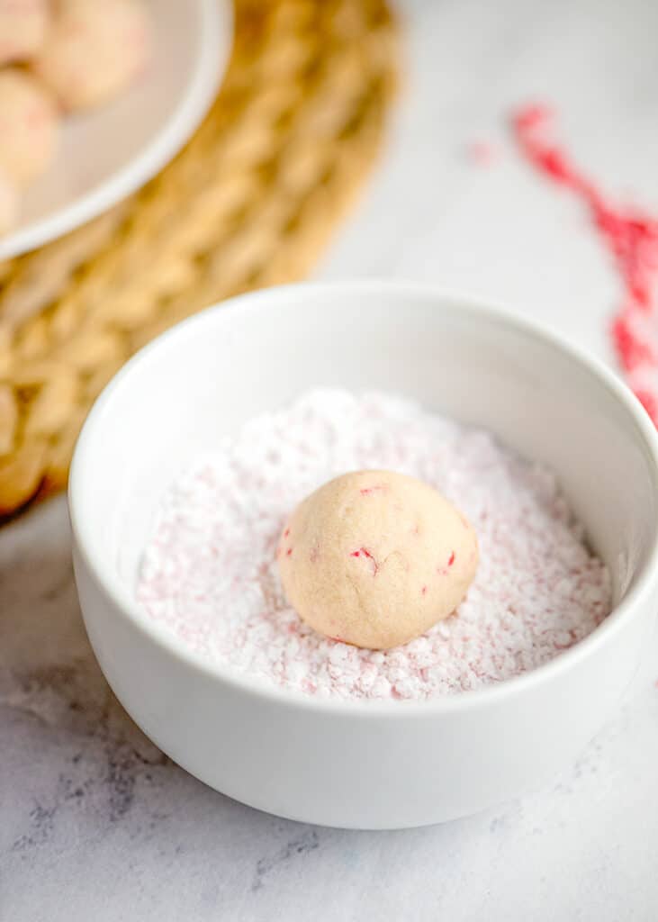 bowl of peppermint crunch and powdered sugar with a baked snowball cookie in it