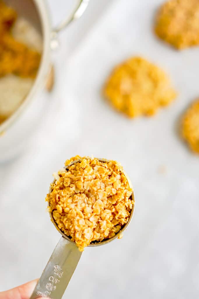 a ¼ cup measuring cup over top of a parchment paper full of cookies