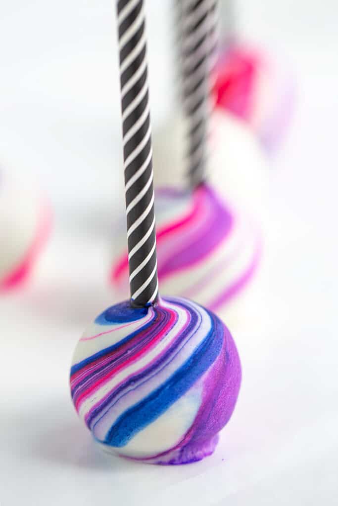 close up of a marbled cake pop with a black and white straw on a white surface