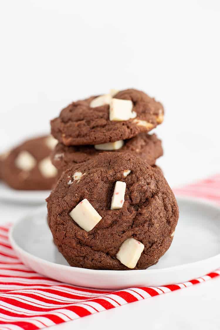 stack of cookies with another cookie leaned on the stack on a white plate with a candy cane striped linen