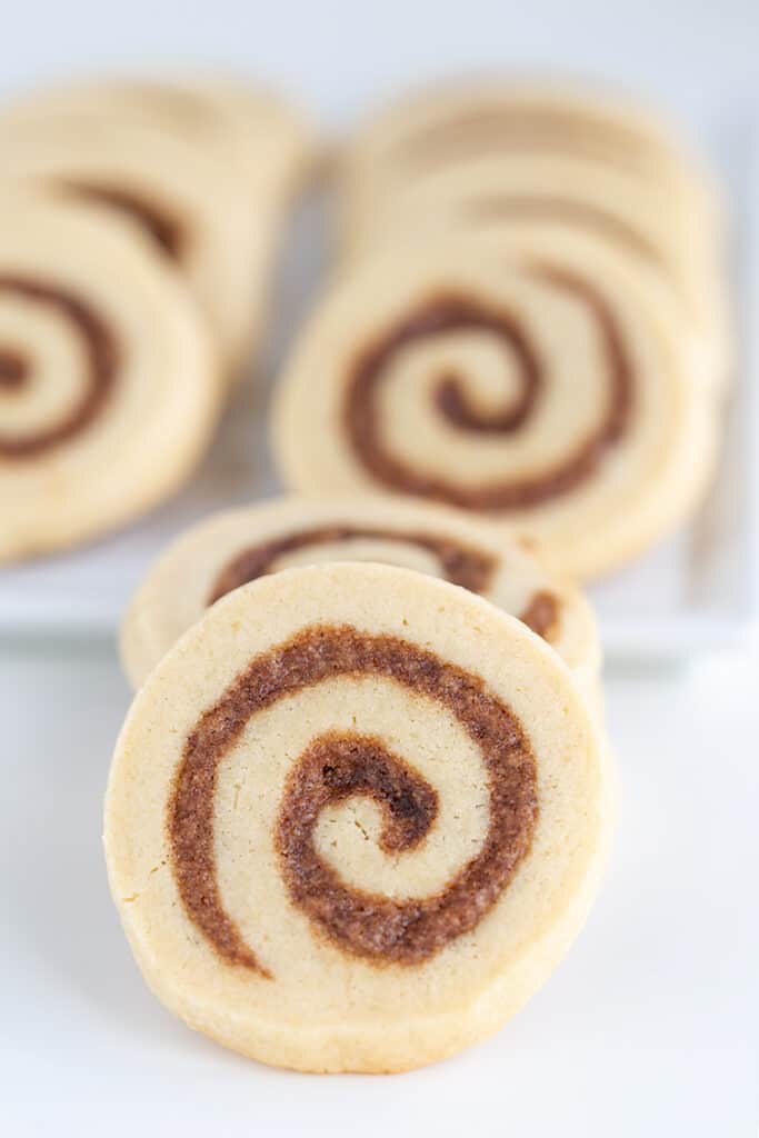 up close photo of the cinnamon roll cookies with a platter of cookies behind it