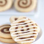 glazed cinnamon roll cookie on a white plate with other cookies behind it