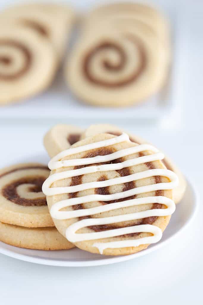 glazed cinnamon roll cookie on a white plate with other cookies behind it