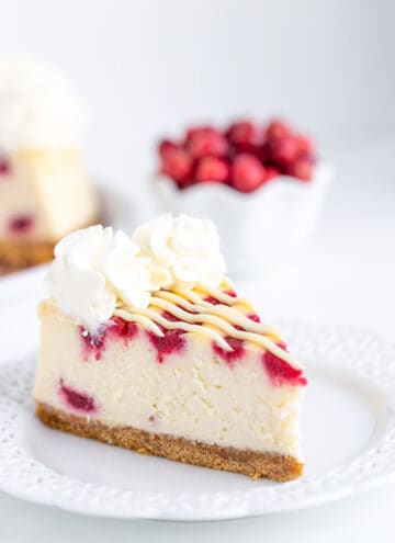 cheesecake on a white lace plate with cranberries behind the cheesecake