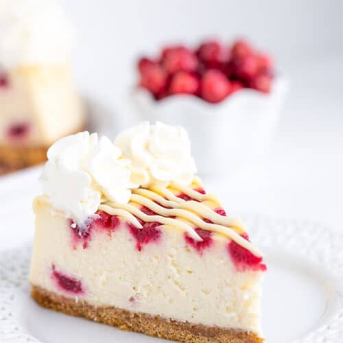 cheesecake on a white lace plate with cranberries behind the cheesecake