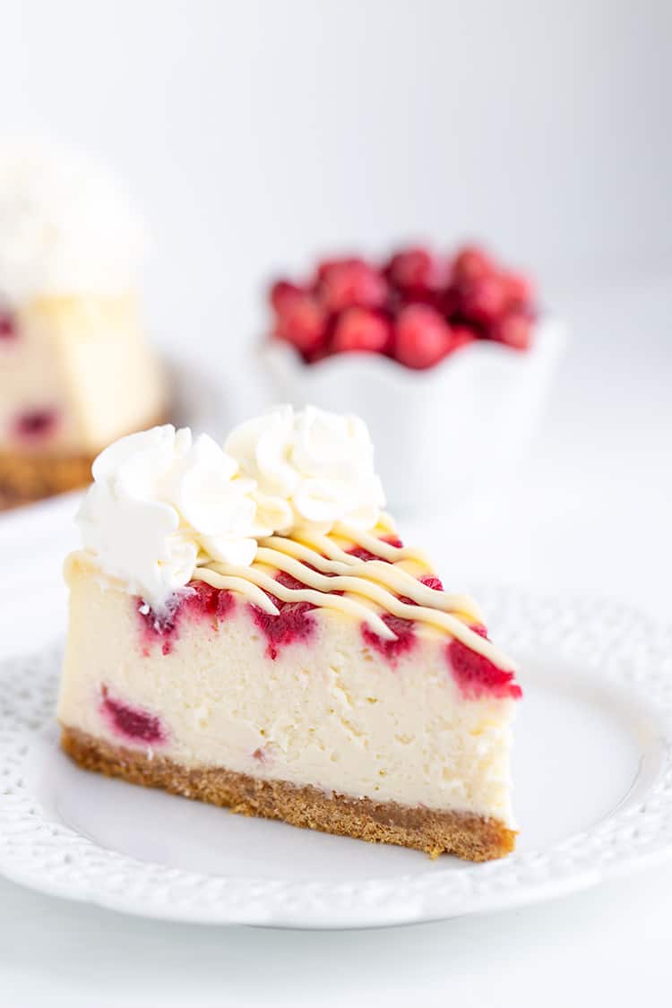 cheesecake on a white lace plate with cranberries behind the cheesecake