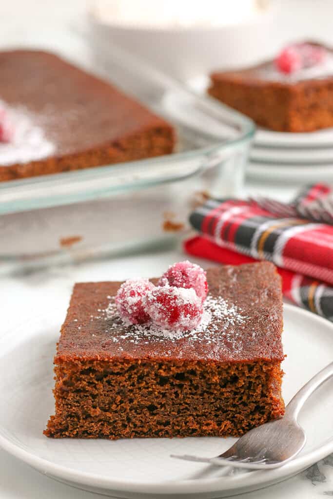 Gingerbread cake on a white plate with plaid linen behind the cake