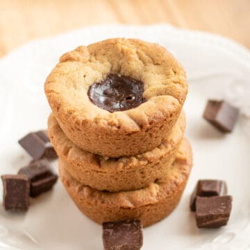 stack of cookie cups with showing the cookie tops with the ganache on a white plate with pieces of chocolate