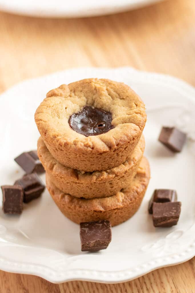 stack of cookie cups with showing the cookie tops with the ganache on a white plate with pieces of chocolate