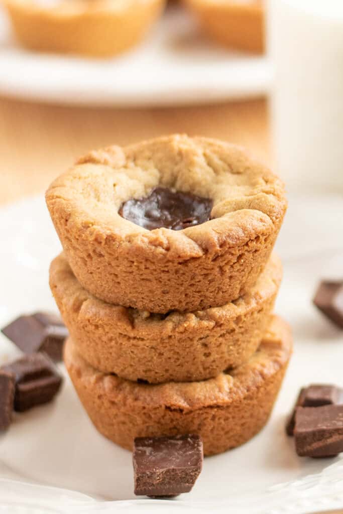 stack of peanut butter cookie cups with pieces of chocolate around it on a white plate