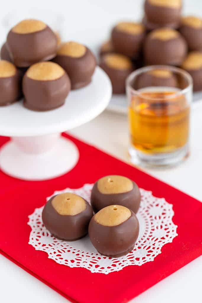 whiskey balls sitting on a doily on a red fabric with a shot glass behind it