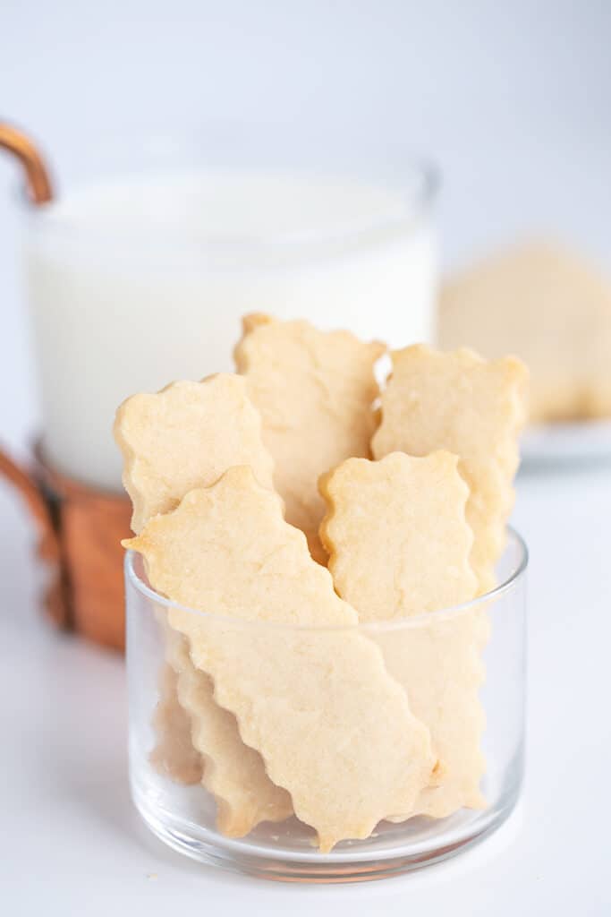 glass bowl with shortbread cookies in it with a glass of milk behind it