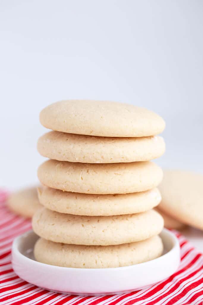 stack of unfrosted sugar cookies on a white plate with a red and white fabric