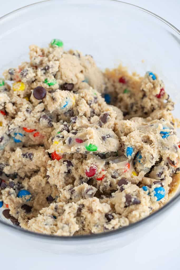 cookie dough with chocolate chips and M&M's in a glass bowl on a white surface