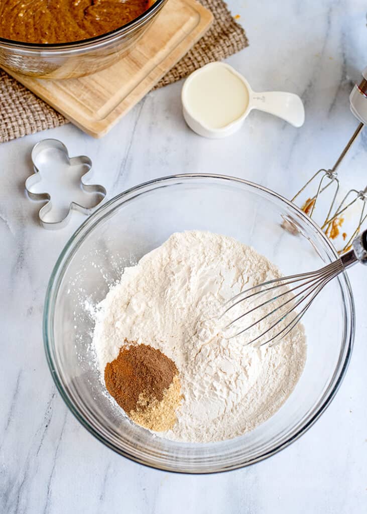 adding dry ingredients to a glass mixing bowl on a marbled background