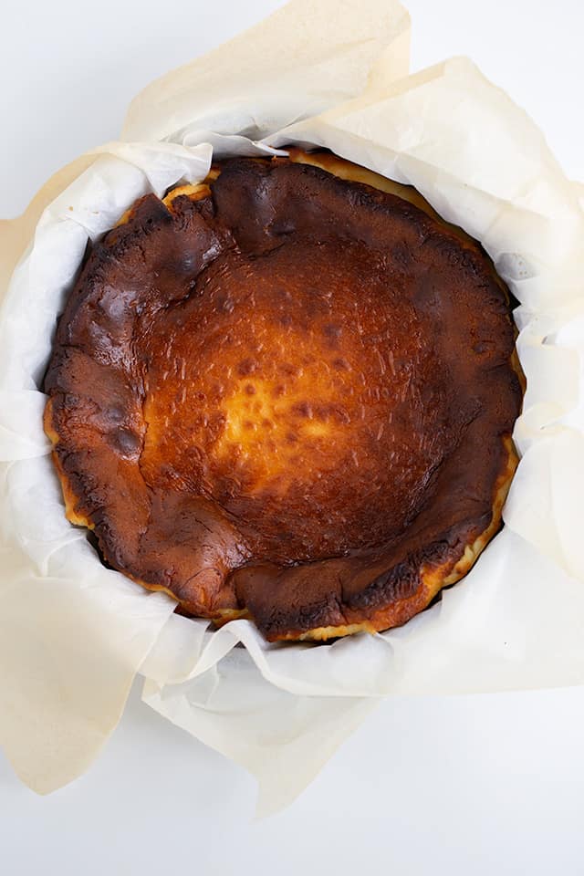 overhead photo of cheesecake on a pan with parchment paper on a white surface