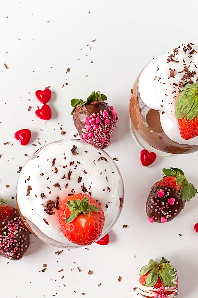 overhead photo of chocolate mousse in glasses with whipped and a strawberry on top on a white surface