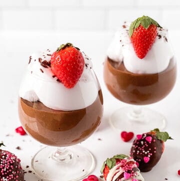 cups of chocolate mousse on a white surface with sprinkles and chocolate covered strawberries