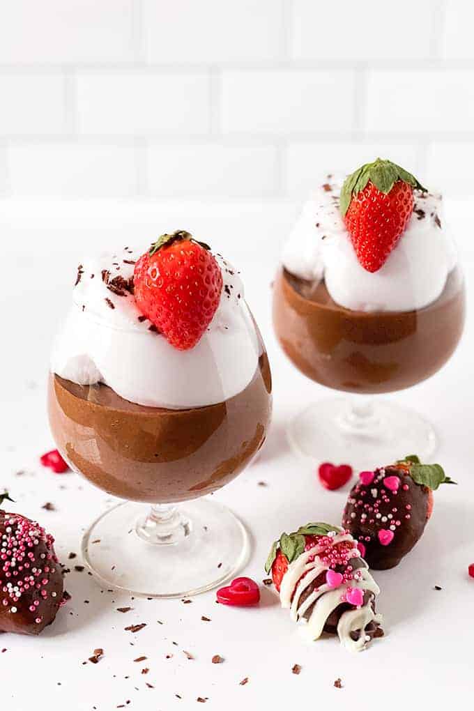 cups of chocolate mousse on a white surface with sprinkles and chocolate covered strawberries