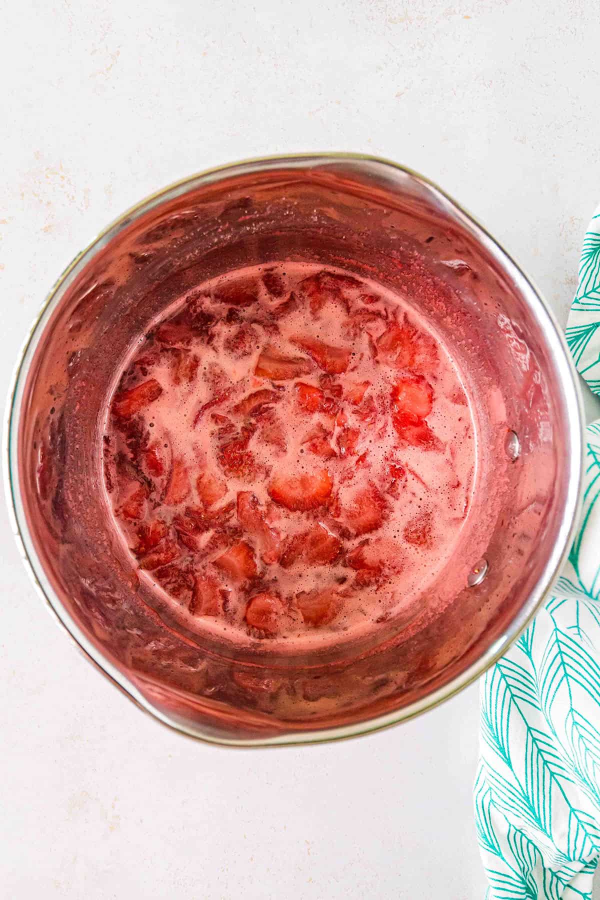 A pot filled with simmering sliced strawberries in liquid, likely being cooked into a sauce or compote—perfect for drizzling over a classic strawberry swirl cheesecake.