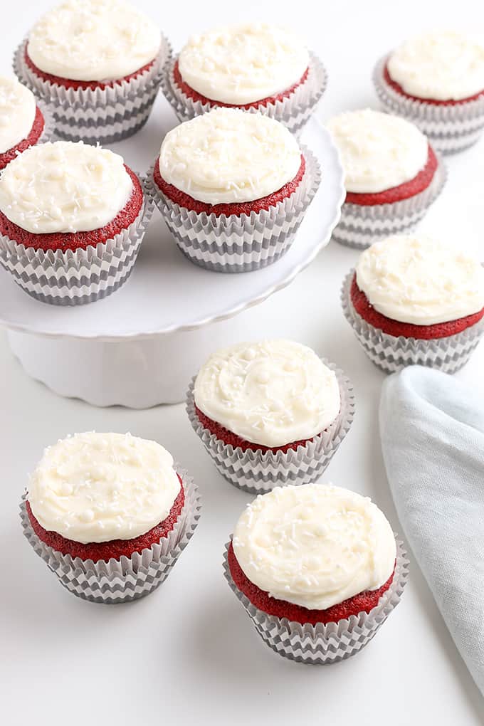 cupcakes on a white surface with a piece of fabric and cupcakes on a white cake plate