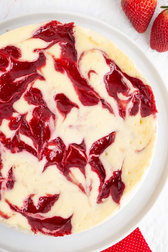 overhead photo of strawberry cheesecake on a large white plate with a red fabric under it