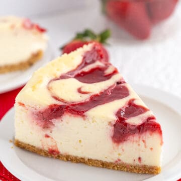 a slice of cheesecake with a strawberry swirl on top on a small white plate