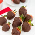 chocolate covered strawberries on a white plate with additional strawberries behind it