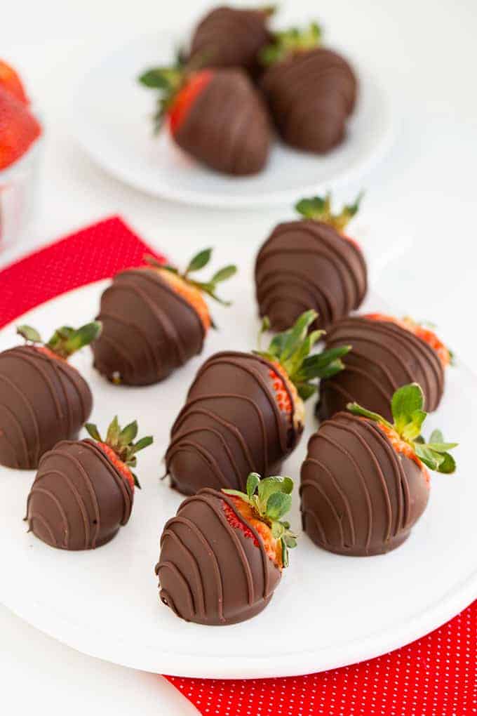 chocolate covered strawberries on a white plate with additional strawberries behind it