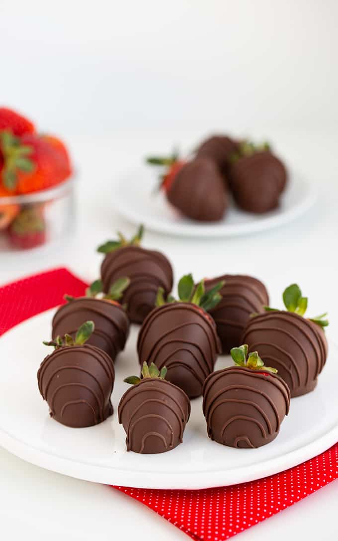 strawberries on a white platter on a red linen with more strawberries behind the platter