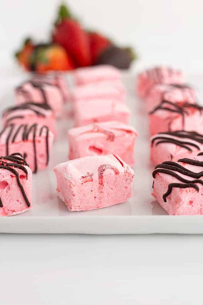 squares of pink marshmallows on a white platter with strawberries behind it