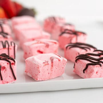 strawberry flavored marshmallows on a white tray with strawberries behind the marshmallows