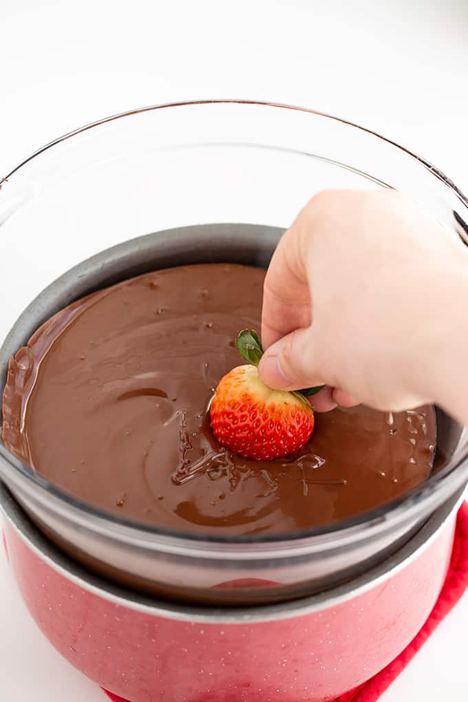 dipping strawberries into a big bowl of melted chocolate chips