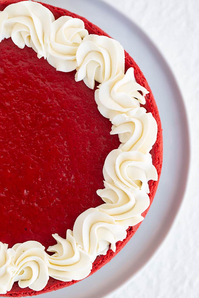 overhead photo of red velvet cheesecake on a white plate with swirls of whipped cream