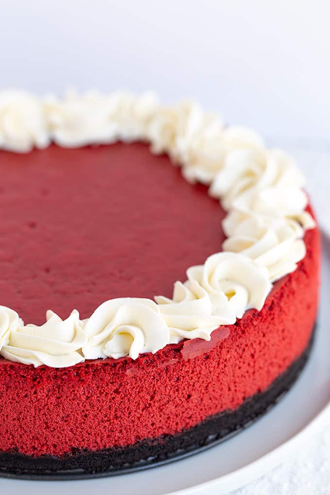 whole red velvet cheesecake on a large white plate with a white background