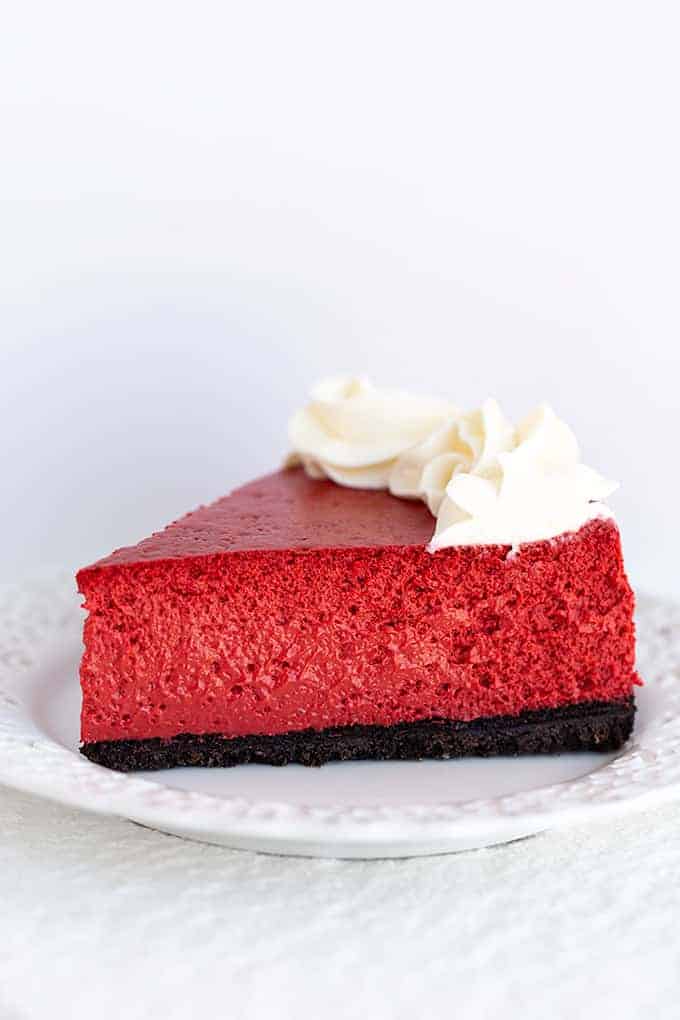 slice of red cheesecake on a white plate on a white background