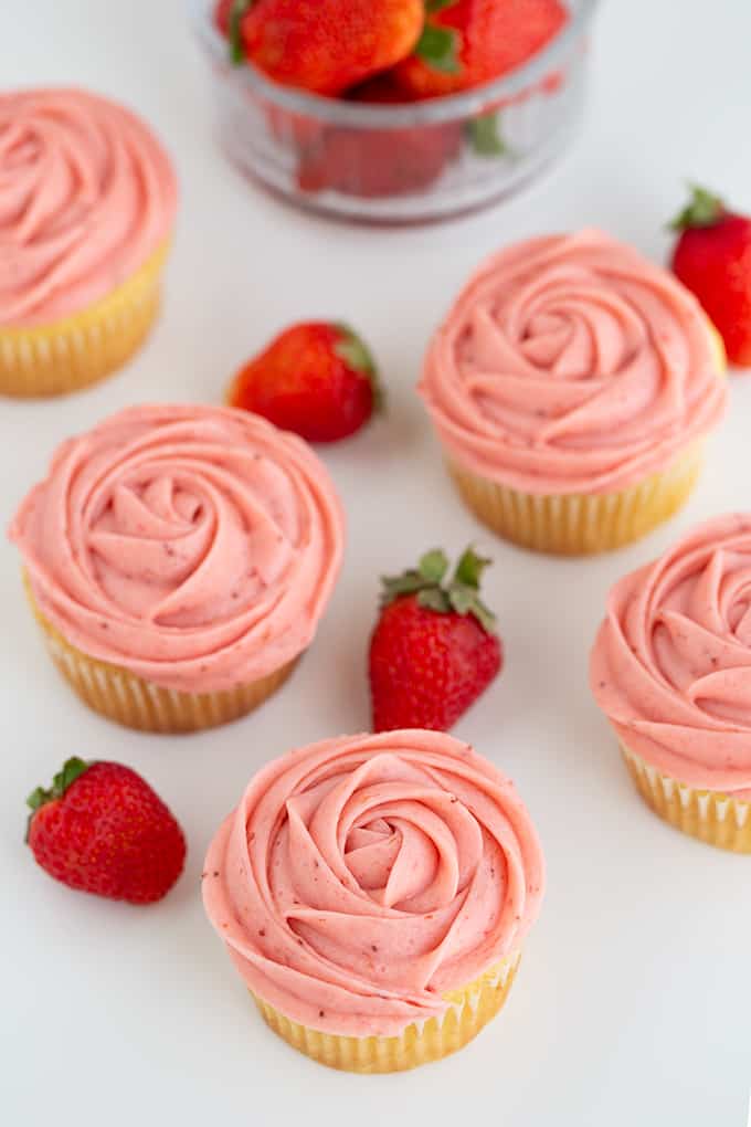 showing the rose swirls piped with frosting on cupcakes on a white surface with fresh strawberries scattered