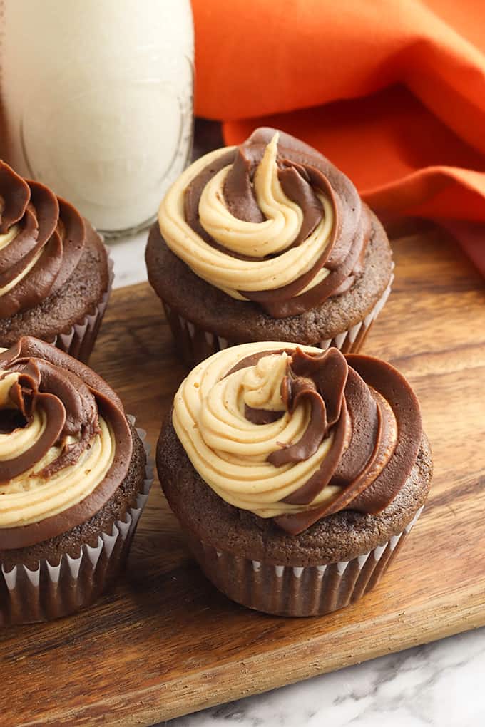 cupcakes on a cutting board with a glass of milk and orange linen behind them