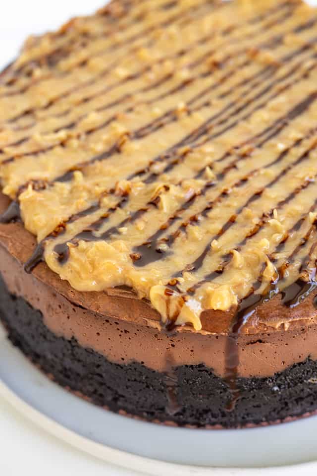 showing the topping on the german chocolate cheesecake and the side of the cheesecake sitting on a white plate 