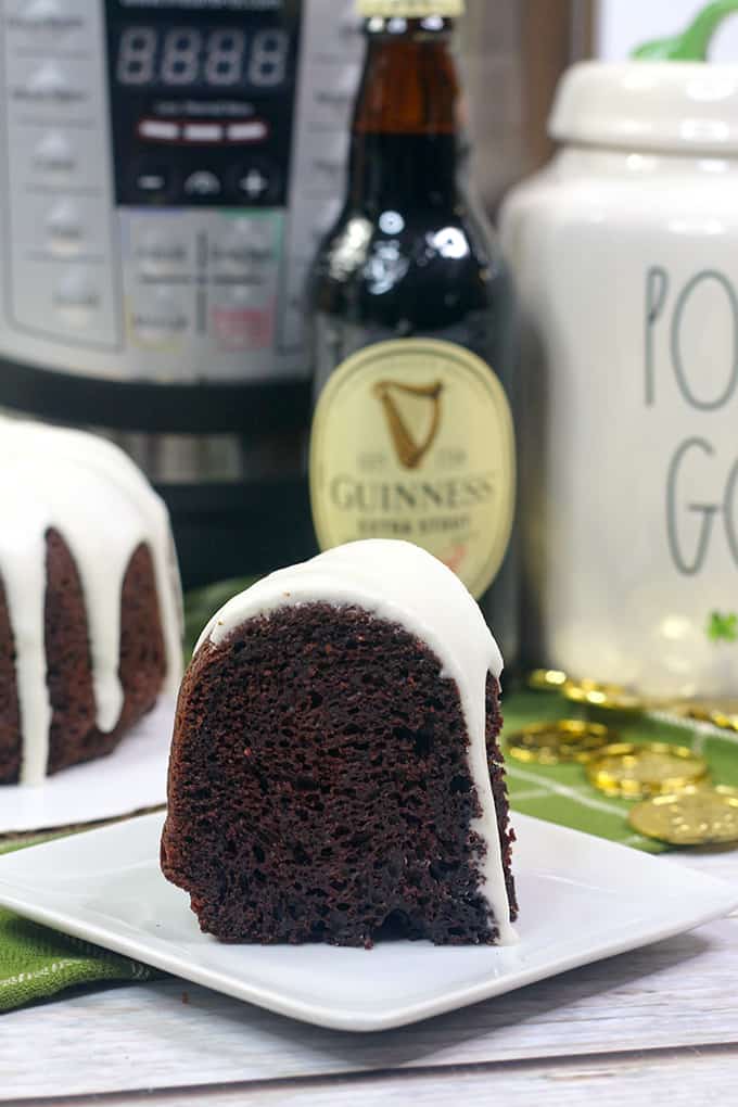 slice of bundt cake on a white dessert plate with an pressure cooker and bottle of beer behind it
