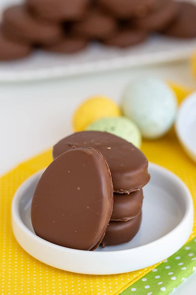 peanut butter eggs stacked with a single egg leaned against the stack on a white plate with speckled eggs behind it