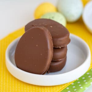 square image of pb eggs stacked on a small rimmed white plate on a yellow fabric with speckled eggs behind it