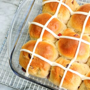 square image of a glass pan full of hot cross buns sitting on a wire rack