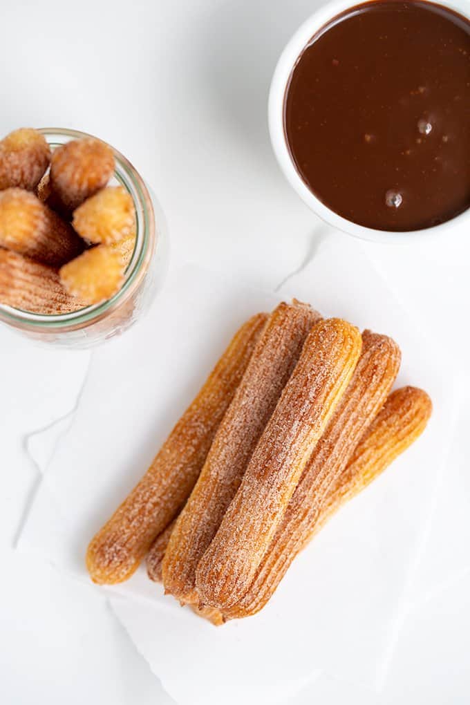 overhead photo of stacked churros on parchment paper with dipping sauce