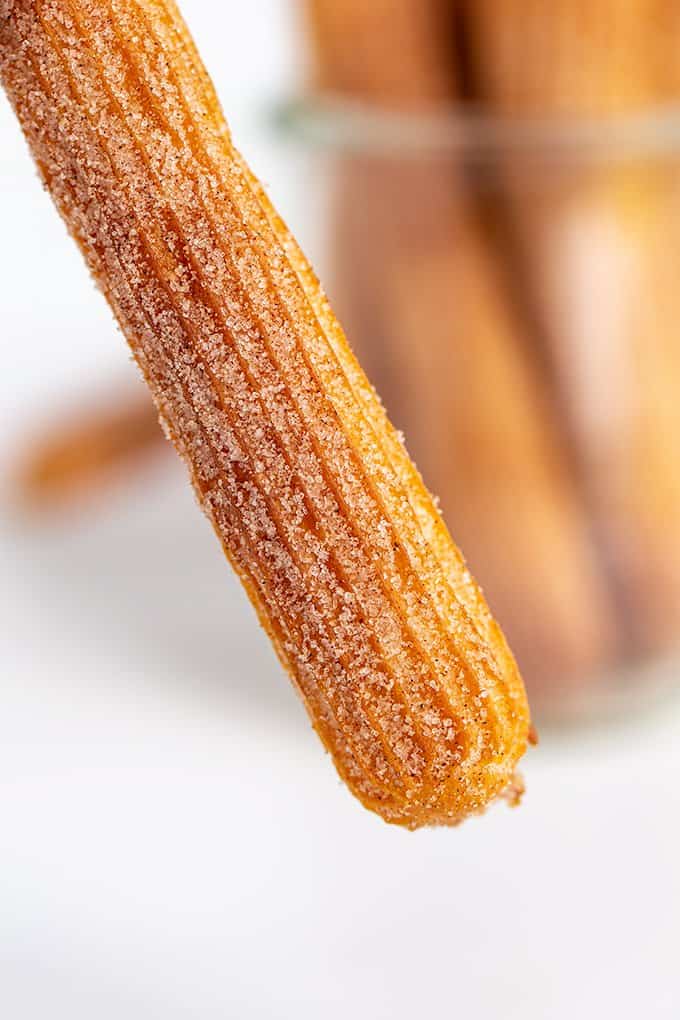 an air fryer churro being held in front of a jar of churros