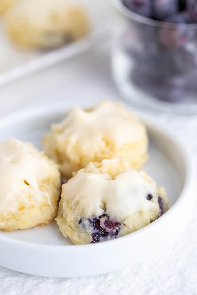 cheesecake cookies on a small white plate with a bowl of blueberries behind it