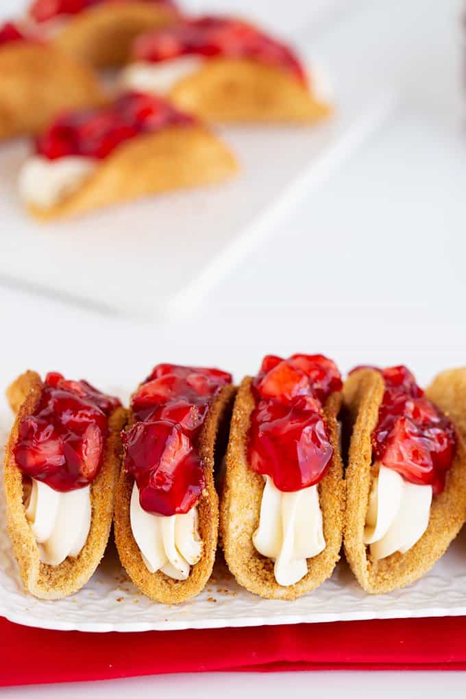 tacos lined up on a small white rectangle plate with a red fabric under it on a white surface