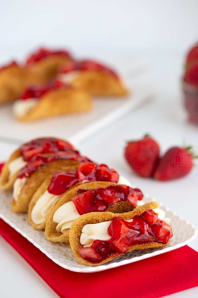 a plate of mini cheesecake tacos on a white plate with a red linen under it
