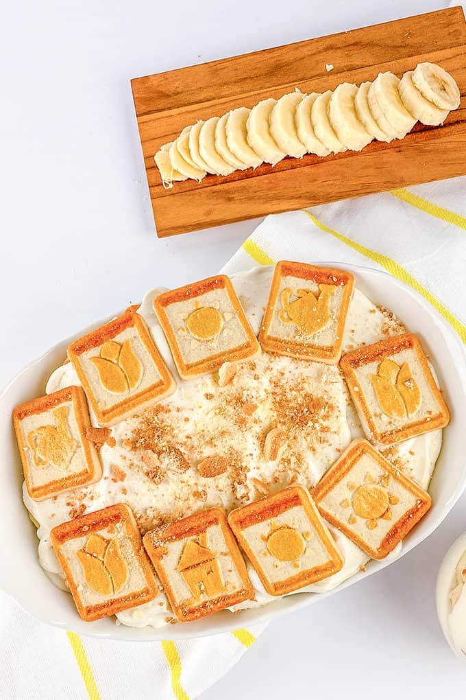 dish full of banana pudding with cookies on top and a board with sliced bananas